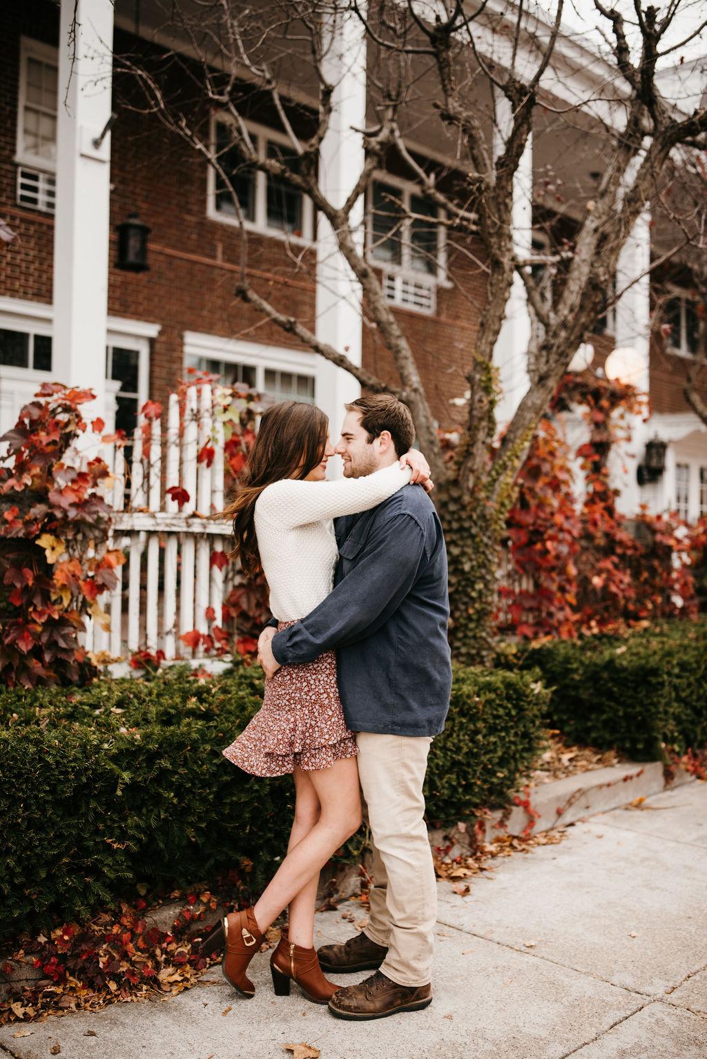 Engagement pictures of Garrett and Morgan in front of a brick building. They are touching noses and hugging.