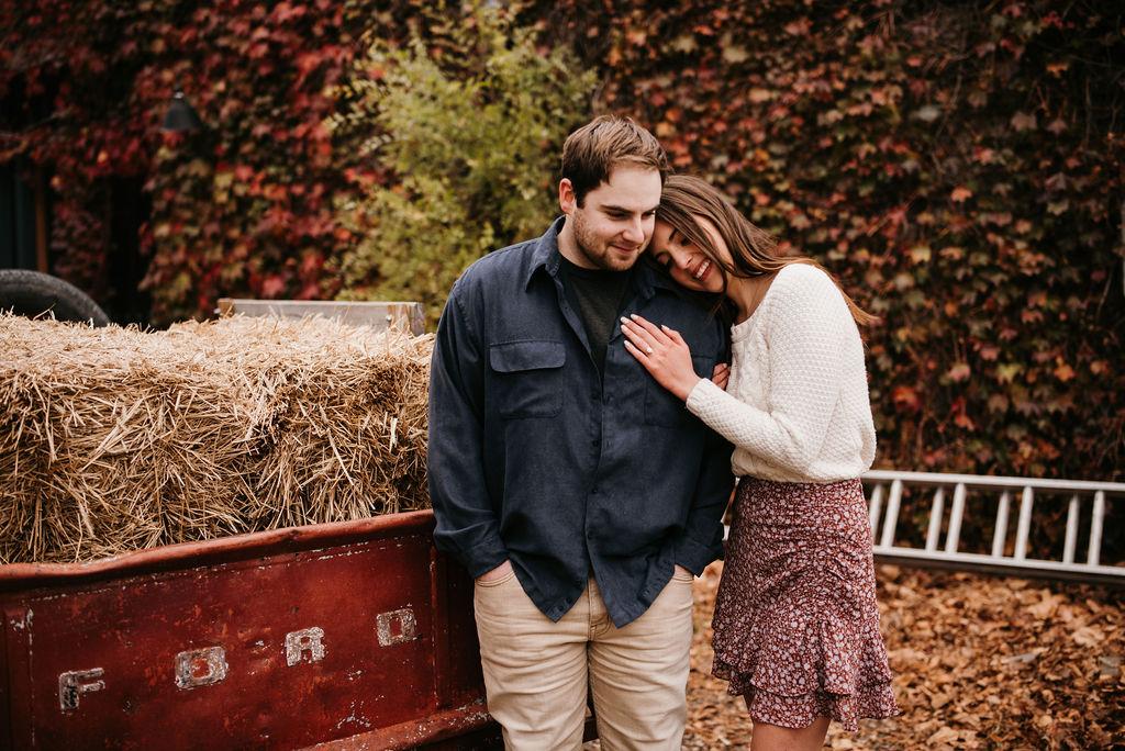 Engagement pictures of Garrett and Morgan standing in front of an ivy wall and an old truck. Morgan is leaning her head on Garrett's shoulder.
