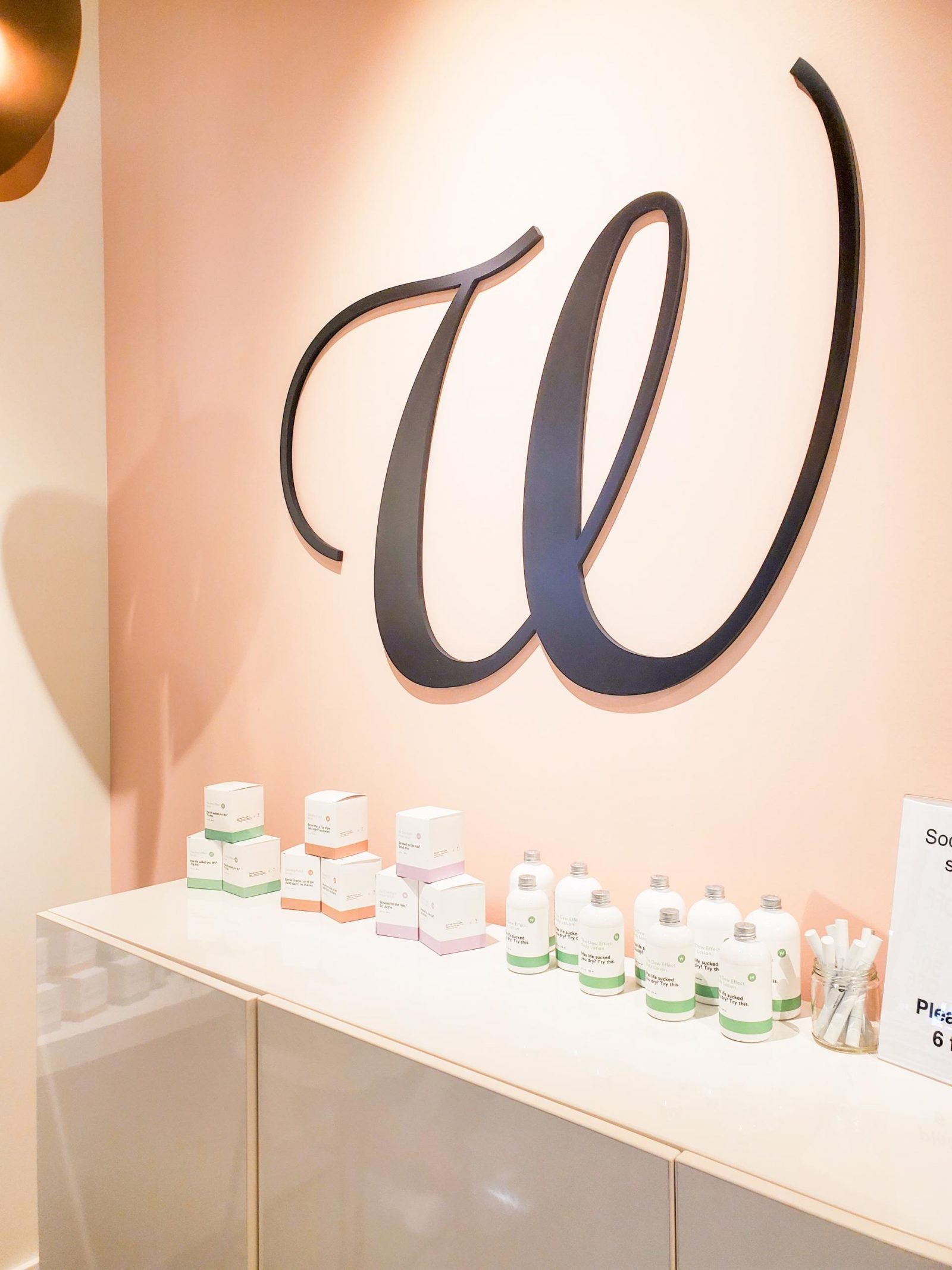 The W Nail Bar logo on a pink wall above an array of their lotions and other products
